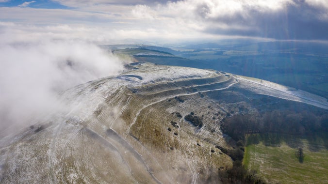 An aerial view of Hambledon Hill, Dorset covered with a thin layer of snow and low clouds